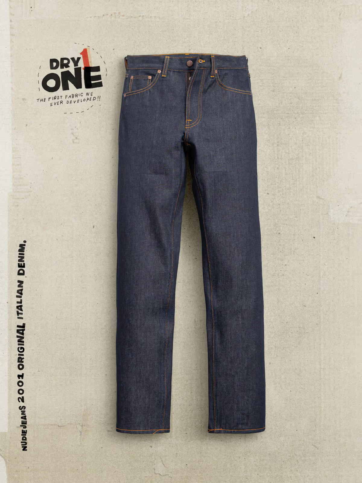 A pair of dark blue denim jeans laid flat against a textured light beige background, with branding text 'DRY ONE' and 'NUDIE JEANS 2001 ORIGINAL ITALIAN DENIM' printed on the left side.