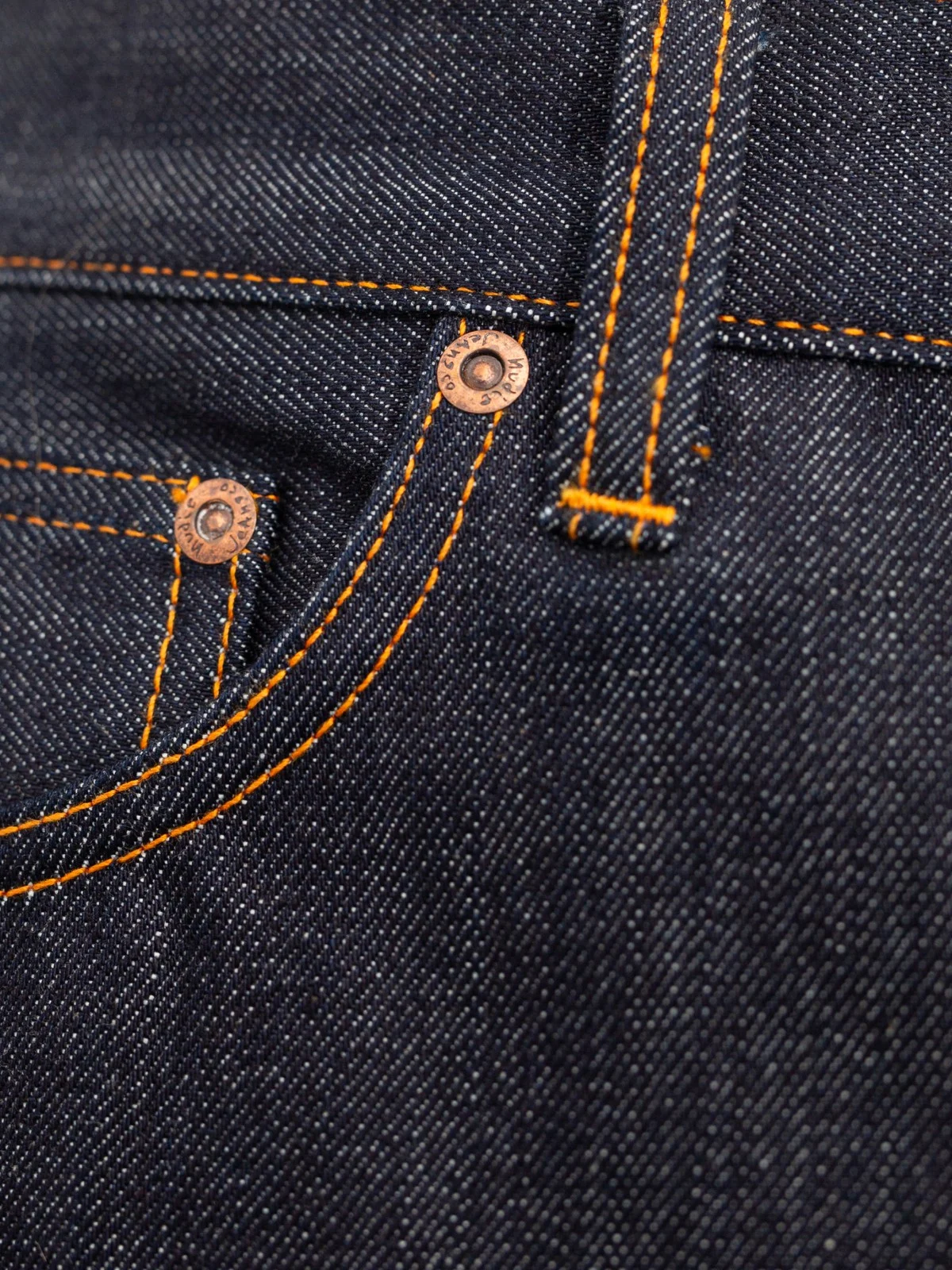 Close-up of dark indigo denim fabric with bright orange contrast stitching and copper-toned metal rivets.
